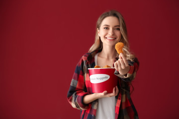 Poster - Beautiful woman with bucket of tasty nuggets on color background