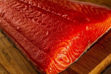 Large fillet cut of dark red Atlantic Salmon isolated on a wood background 