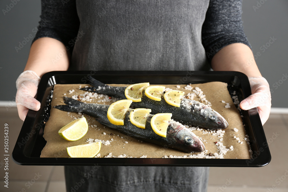 Woman holding baking sheet with raw seabass fish, closeup