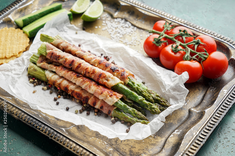 Tray with tasty bacon wrapped asparagus and vegetables on table