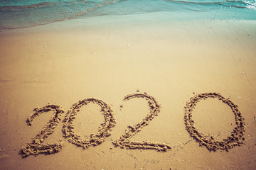 Happy New Year 2020 concept, 2020 number lettering on the sea beach, wave and golden light of sunset.