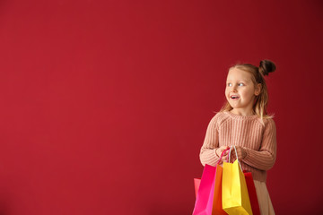 Cute little girl with shopping bags on color background