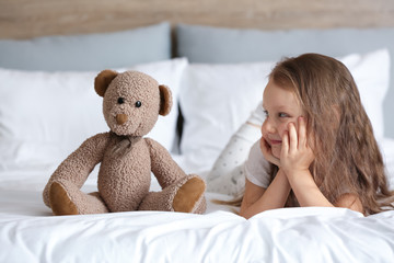 Wall Mural - Cute little girl with toy bear lying on bed