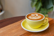 © visitr - Hot cappuccino coffee in a yellow cup with latte art on the wooden table in the coffee shop.