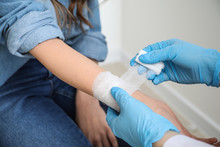 Doctor Applying Bandage Onto Wrist Of Young Woman, Closeup