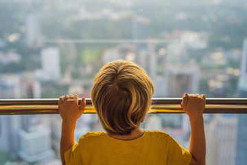 Wall Mural - Little boy looks at Kuala lumpur cityscape. Panoramic view of Kuala Lumpur city skyline evening at sunset skyscrapers building in Malaysia. Traveling with kids concept