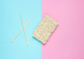 Raw instant noodles and chinese chopsticks on pastel background, minimalism