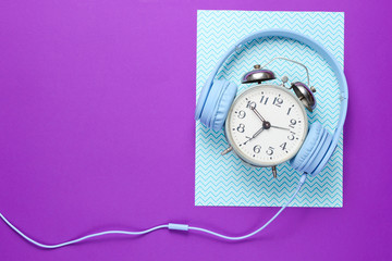 Sticker - Time listen to music concept. Retro alarm clock with wired headphones on purple blue creative background. Top view