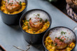 Orange pumpkin risotto with scallop and foamy sauce in black bowl on rustic wooden table