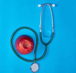 green medical stethoscope and ripe red apple