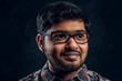 © Fxquadro - Close-up portrait of a young Indian guy in eyewear and checkered shirt in studio against the background of the dark wall