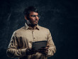 © Fxquadro - Portrait of a smart Indian male in eyewear and shirt holding a tablet computer and looking sideways in studio against the background of the dark wall.