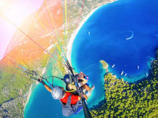 Paragliding in the sky. Paraglider tandem flying over the sea with blue water and mountains in bright sunny day. Aerial view of paraglider and Blue Lagoon in Oludeniz, Turkey. Extreme sport. Landscape