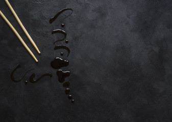 Chopsticks with leaking soy sauce on black table.