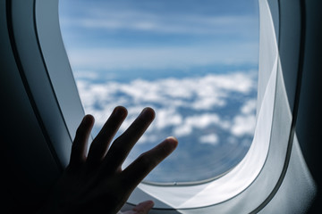 Wall Mural - View from airplane window. Aerial landscape. Flying over clouds. Hand touching the glass