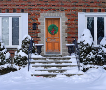 Snow Covered Front Steps Of Brick House With Elegant Wooden Door With Christmas Wreath