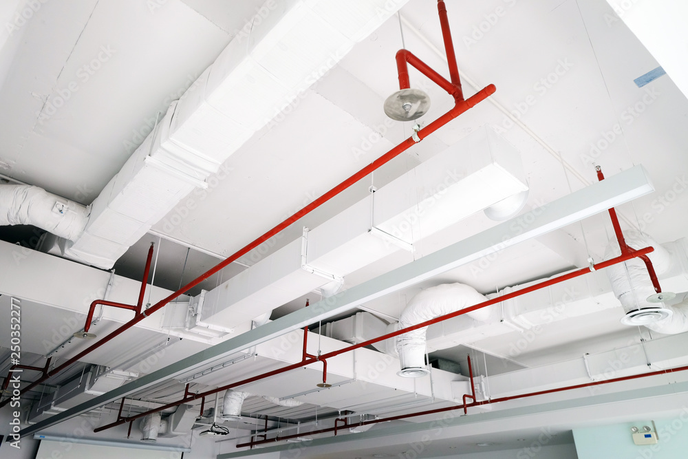 Perspective view of white air duct on the ceiling with red water sprinkler pipe - obrazy, fototapety, plakaty 