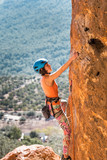 Fototapeta  - A girl in a helmet climbs a rock.