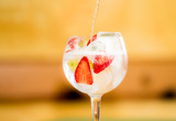 Preparación a chorro de coctel gintonic de ginebra y tónica con fresas y uvas en fondo cálido desenfocado