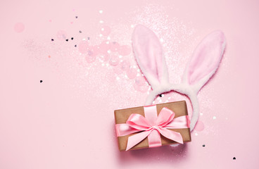 Top view and flat lay of Easter symbol - bunny ears and gift box on pink background. Festive and bright, confetti and sparks. Easter greetings