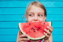 Little Girl Eating A Ripe Juicy Watermelon Over Blue Plank Wall Background