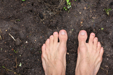 barefoot man stands on empty black soil ground in spring, poster for ecology fitness, concept poverty, top view, closeup