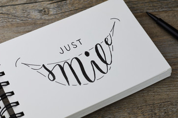 JUST SMILE hand lettering in notepad on wooden background