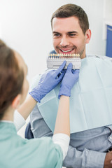 Wall Mural - selective focus of cheerful man smiling near dentist with teeth color palette in hands