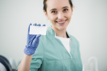 Wall Mural - selective focus of blank card in hand of cheerful female dentist