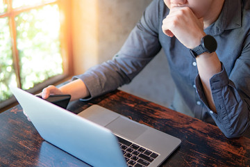 Young Asian businessman or male entrepreneur using laptop computer and smartphone while working in the cafe. Mobile app or internet of things concepts. Modern lifestyle in digital age.