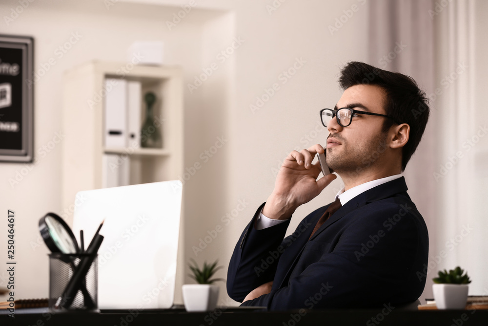 Handsome young businessman talking by mobile phone in office