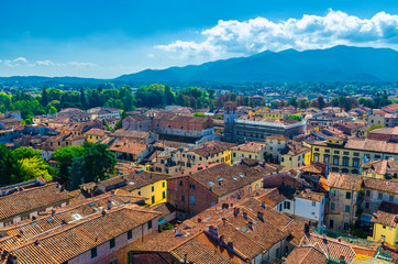 Aerial top panoramic view of historical centre medieval town Lucca with old buildings, typical orange terracotta tiled roofs and mountain range, hills, blue sky white clouds background, Tuscany, Italy