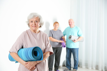 Wall Mural - Elderly woman with yoga mat indoors. Space for text