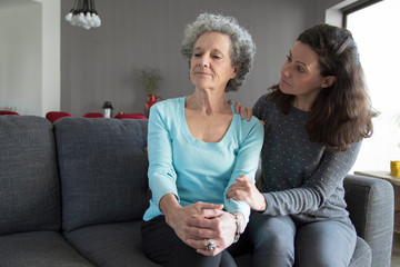 Lady holding hand on senior mother shoulder and supporting her