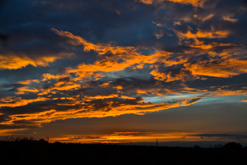 Wall Mural - Beautiful orange clouds reflecting sunset colors above dark landscape