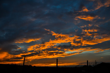 Wall Mural - Beautiful orange clouds reflecting sunset colors above dark landscape