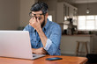 © Cavan Images - Stressed businessman with laptop computer on wooden table sitting at home