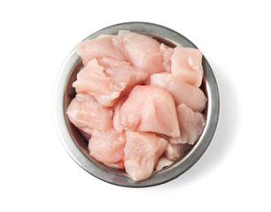 Fresh, raw pet food. Pieces of chicken fillet in a metal bowl, isolated on a white background. Top view.