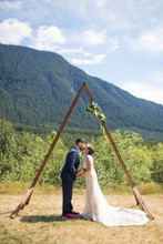 Side View Of Newlywed Couple Kissing While Standing Against Mountain In Wedding Ceremony