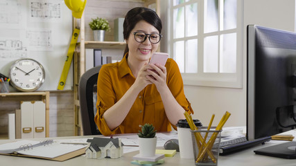 Wall Mural - happy girl interior designer taking break in afternoon tea time using cellphone chatting online smiling. female architect relax in office texting message cheerfully after project done well.