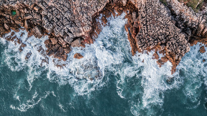 Wall Mural - Drone aerial top view of sea waves hitting rocks on the beach with turquoise sea water. Amazing rock cliff seascape in the Portuguese coastline, Cascais.