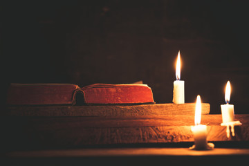 Open Holy Bible and candle on a old oak wooden table. Beautiful gold background. Religion concept.