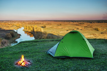 Wall Mural - green tourist tent in green grass of hill above river