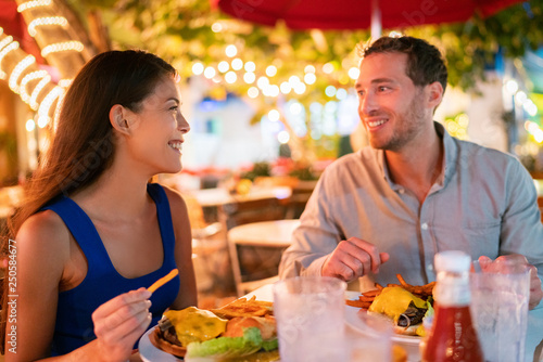 Cuadros en Lienzo Couple eating hamburgers at outdoor restaurant terrace happy tourists on summer vacation