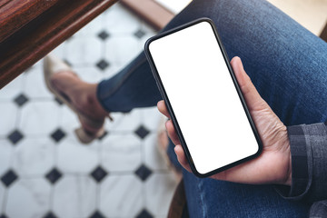 Top view mockup image of a woman holding black smart phone with blank white desktop screen while sitting in cafe