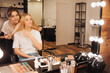 © estradaanton - Nice cheerful young make up artist stand behind blonde model and smile to her in beauty room. she hold her hair and look into mirror. Client point on hair.