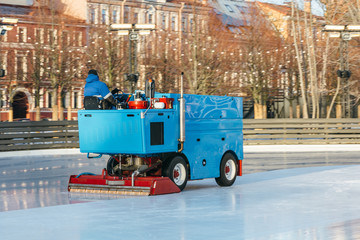 Outdoor photo of special machine leveling ice rink in motion, side view/ ice maintenance machine clean and pours ice before the game, ice resurfacer at work, public skating rink, hockey stadium.