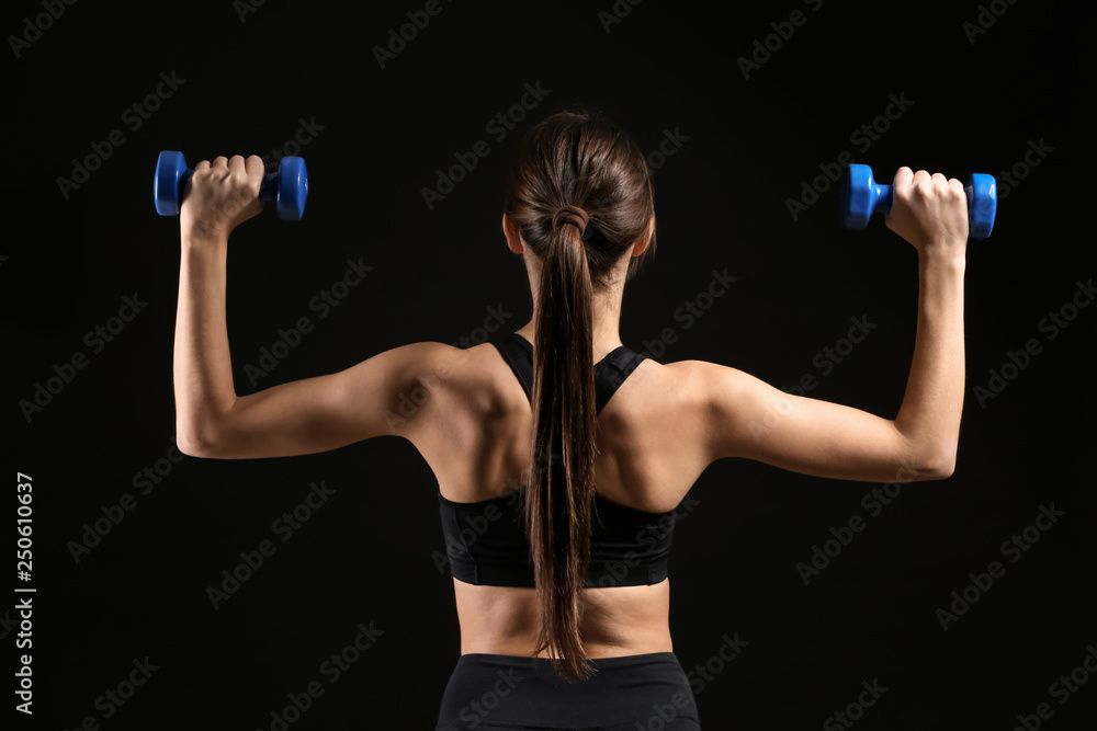 Sporty young woman with dumbbells on dark background
