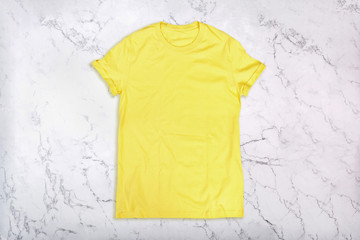 Wall Mural - Yellow t-shirt on white marble background. Flat lay. Top view