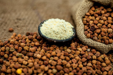 Close up of a jut bag full of chickpeas or grams in it and its floor or besan ka atta in a clay bowl on brown colored surface.